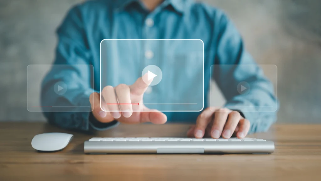 Man sitting at table behind mouse & keyboard, pressing translucent video button